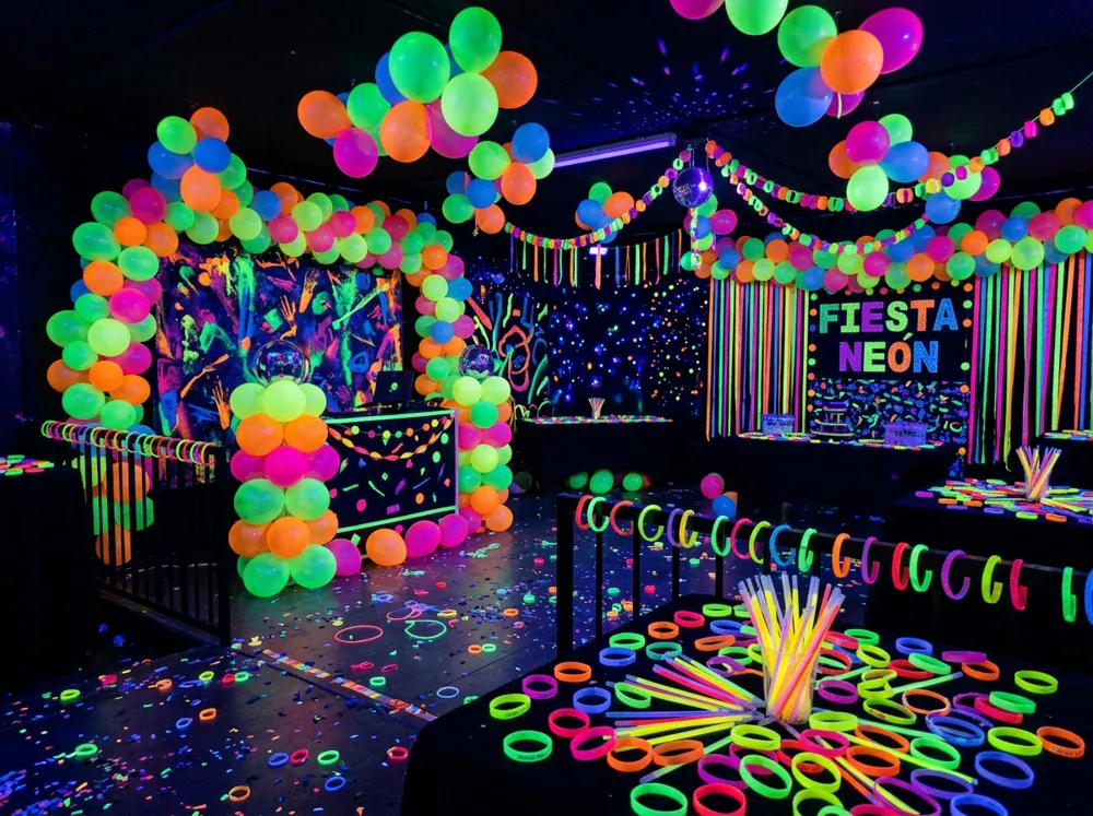 Fiesta de neón con globos fluorescentes, luz negra y personas con pulseras que brillan