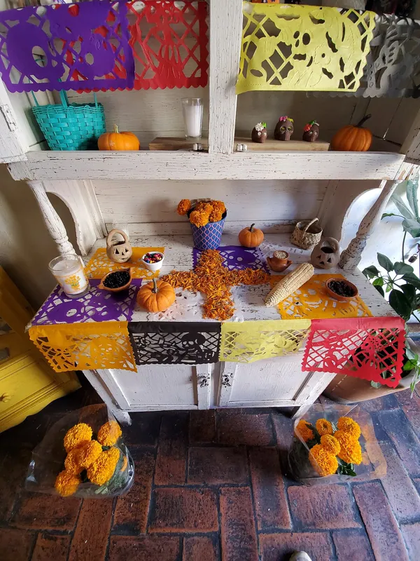 Ofrendas de Día de Muertos con cempasúchil naranja, calaveras de azúcar de colores y papel picado morado y rosa